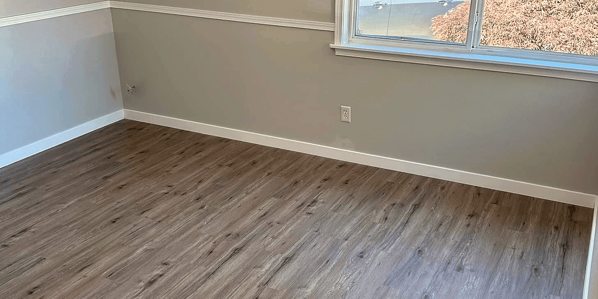 A finished room corner with painted walls, new plank flooring and white baseboard trim.